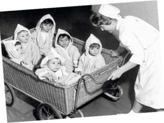 Eine Pflegerin schiebt fünf Kinder in einem großen Kinderwagen.